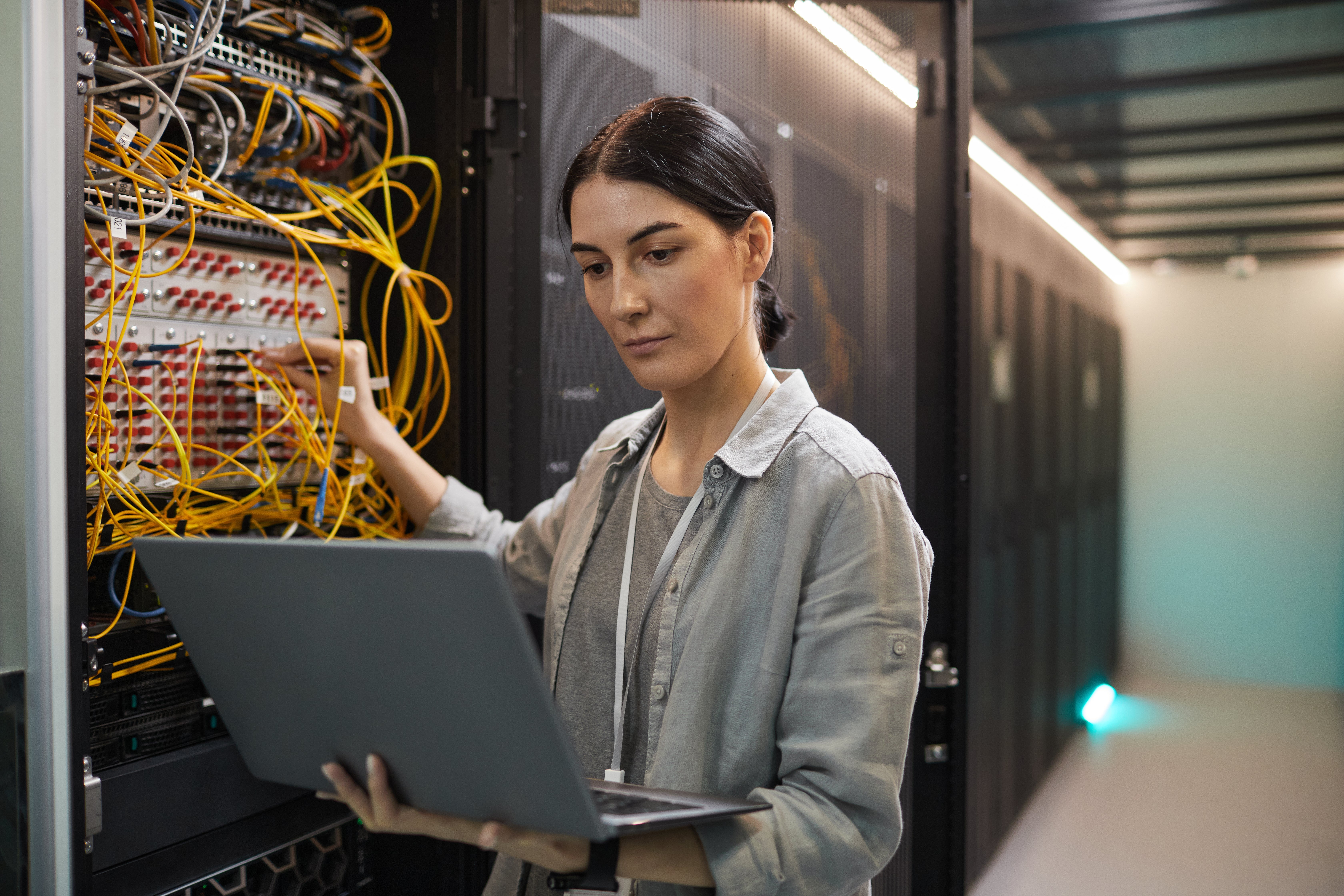 A Female network engineer connecting cables in server cabinet while working with a supercomputer in the data center.