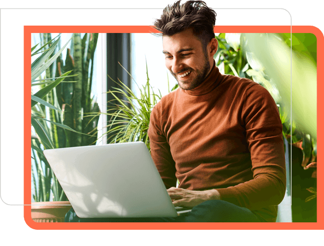 man in orange sweater at laptop with plants